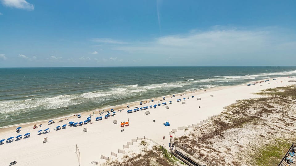 Enjoy the vibrant beach scene with colorful umbrellas and rolling waves under a clear blue sky