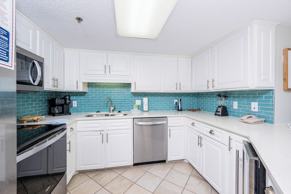 Bright white cabinetry and turquoise tile complement the kitchen, featuring a convenient breakfast bar and coffee station