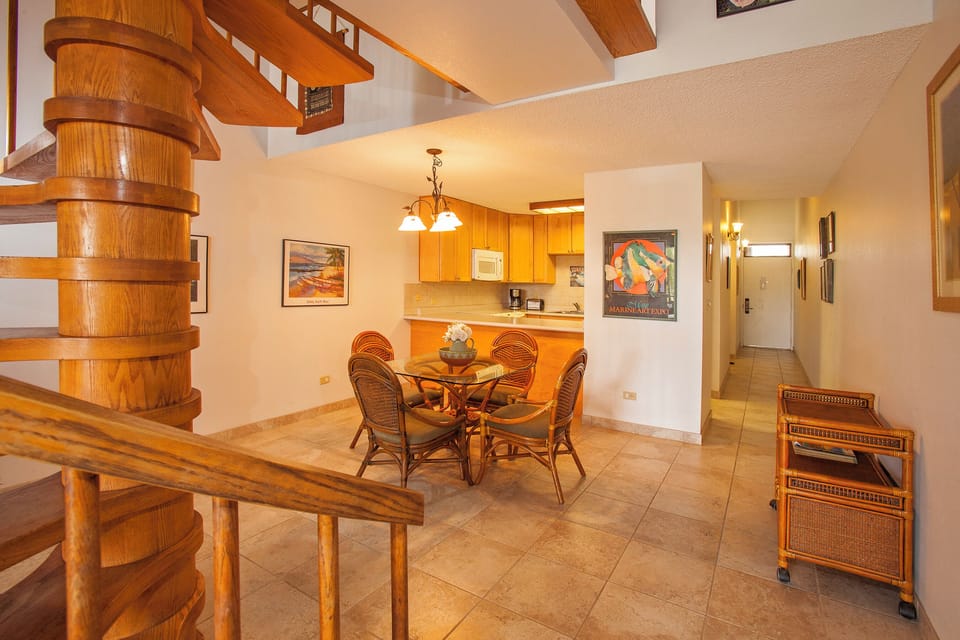 Gather around the intimate dining table beneath warm lighting, where your group can share meals and stories. The open layout connects you to the kitchen and spiral staircase, creating an inviting flow for your stay.