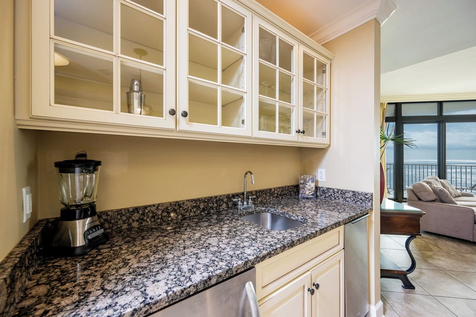 The wet bar features elegant cabinetry with glassware, sleek granite countertops, and ample space for entertaining guests