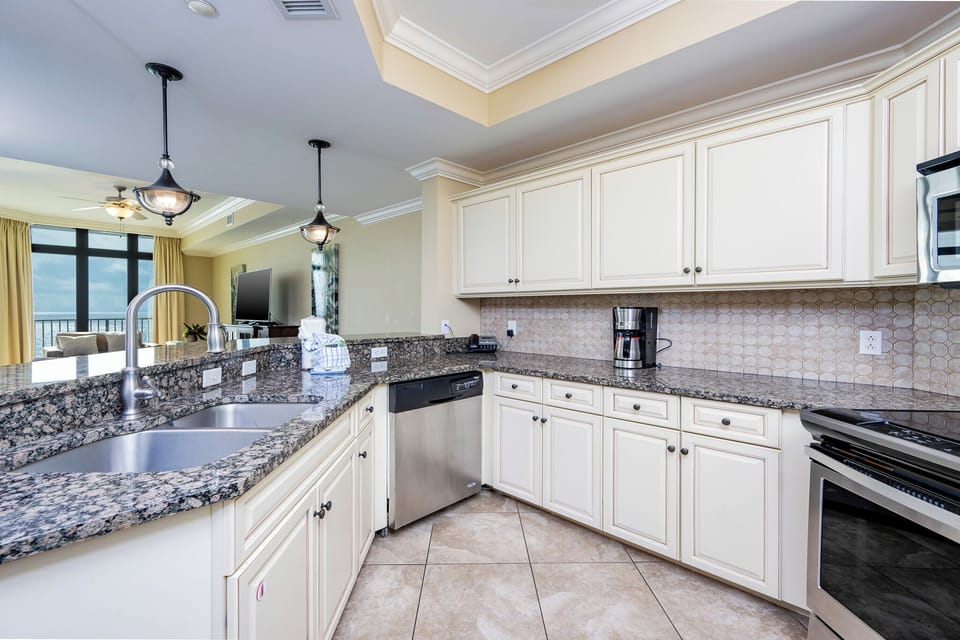 This modern kitchen features granite countertops, stainless appliances, and a coffee maker, with a view of the beach front