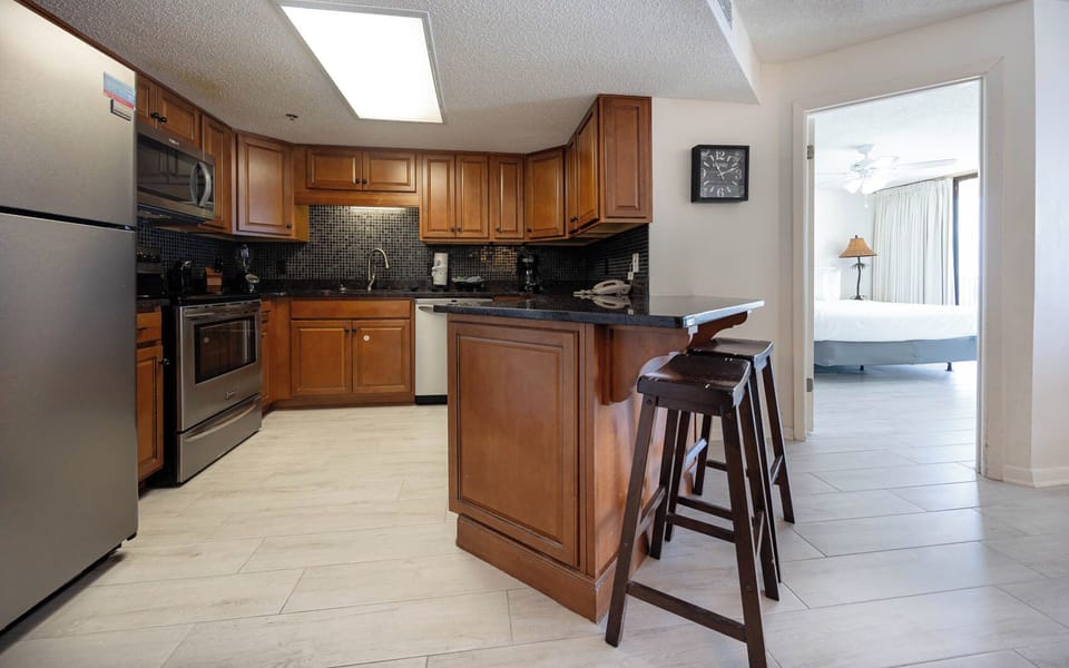 The kitchen features rich wood cabinetry, a sleek breakfast bar, stainless appliances, and dark countertops