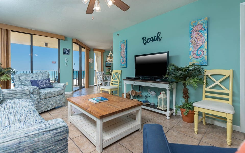 Bright living area with coastal decor, featuring a comfortable sofa with queen sleeper, TV, and a view of the beach