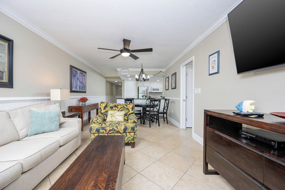 This inviting living area features a comfortable sofa, a mounted TV, and a view of the modern kitchen, perfect for relaxation