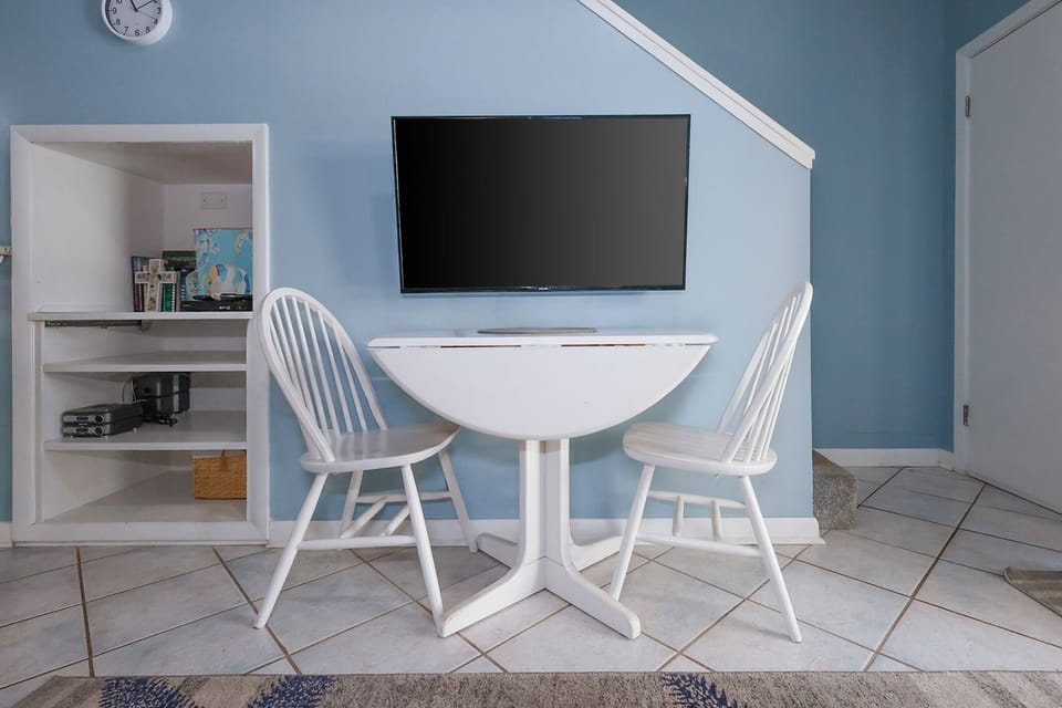 This cozy nook features a wall-mounted TV and a charming round table with two white chairs, perfect for meals or games