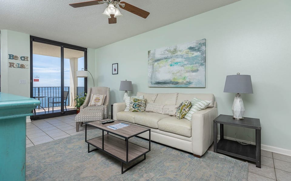 Living area features a light sofa with queen sleeper, a modern coffee table, and stunning views of the beach from the balcony