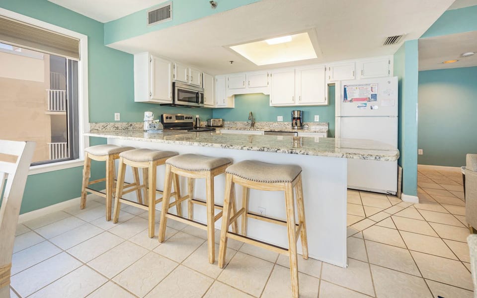 This kitchen features white and stainless appliances, granite countertops, and a cozy breakfast bar with four stools