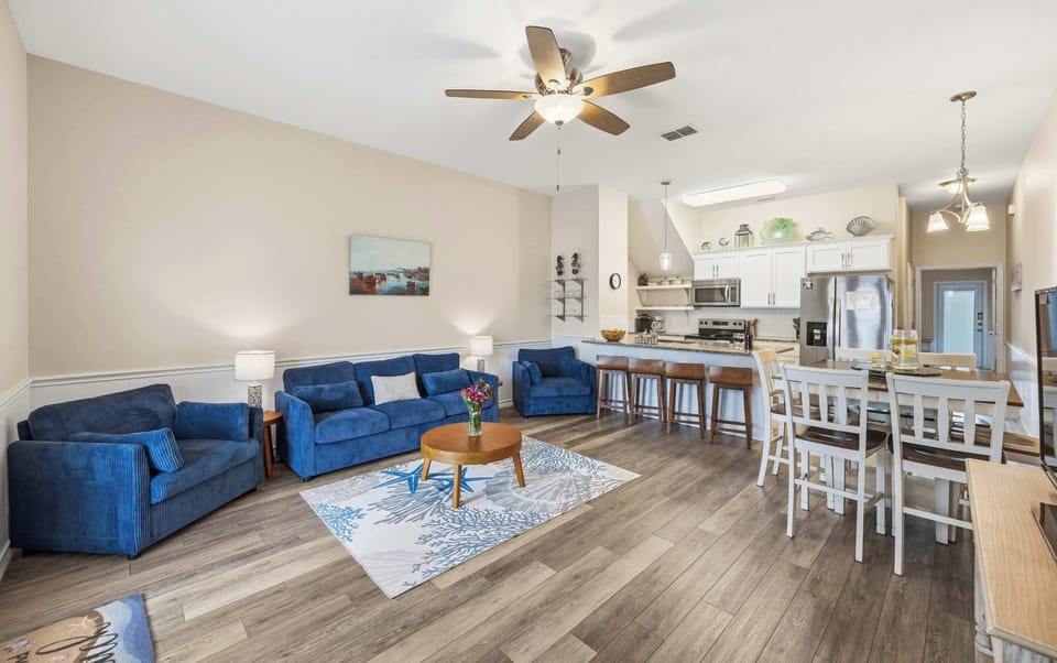 Open Floor Plan — Navy Sofas, Round Coffee Table, Kitchen with Bar Stools & Dining Area