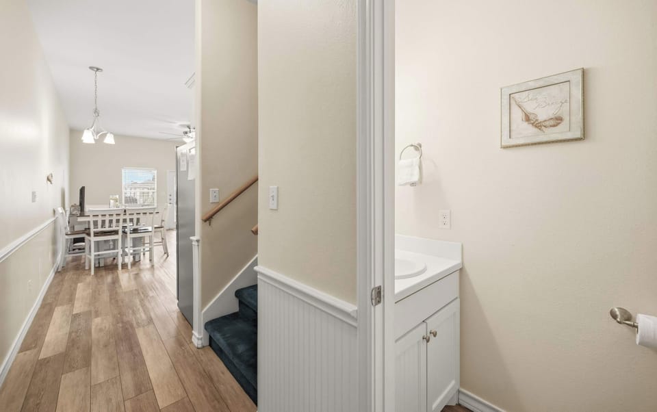 Hallway & Half Bath — Stairs to Upper Level, White Vanity & Sea Breeze Art