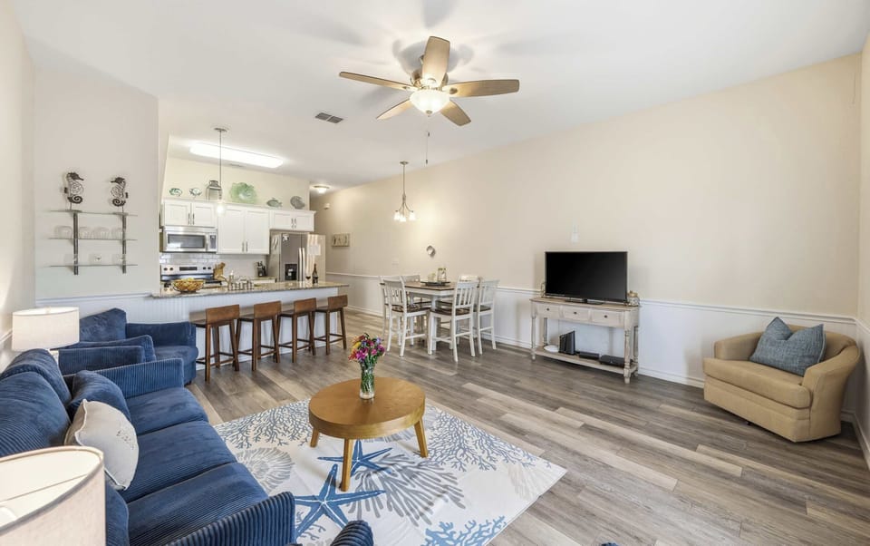 Living Room — Navy Sofa & Chair, Starfish Coral Rug, Round Coffee Table & Open Kitchen with Bar Stools