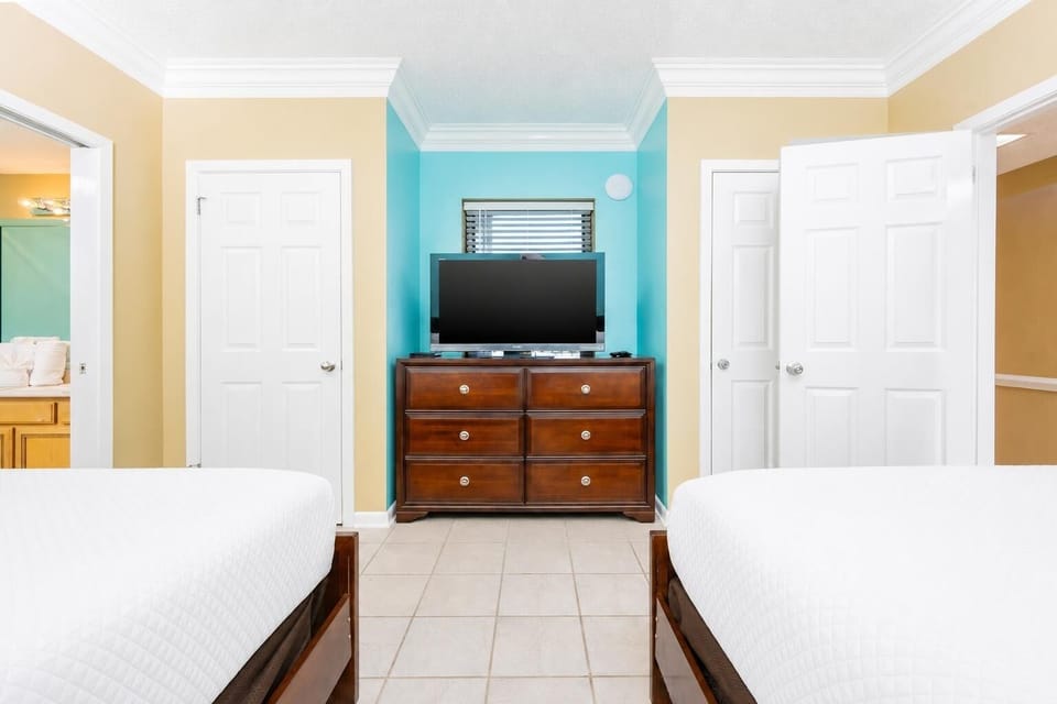 This guest bedroom features two queen beds, a dresser with a flat-screen TV, and colorful walls that create a cheerful vibe
