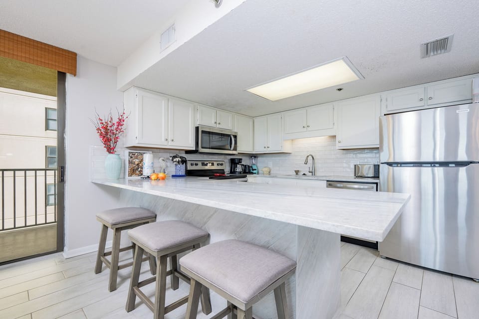 Bright kitchen area featuring white cabinetry, a marbled breakfast bar with seating, and a view of the balcony