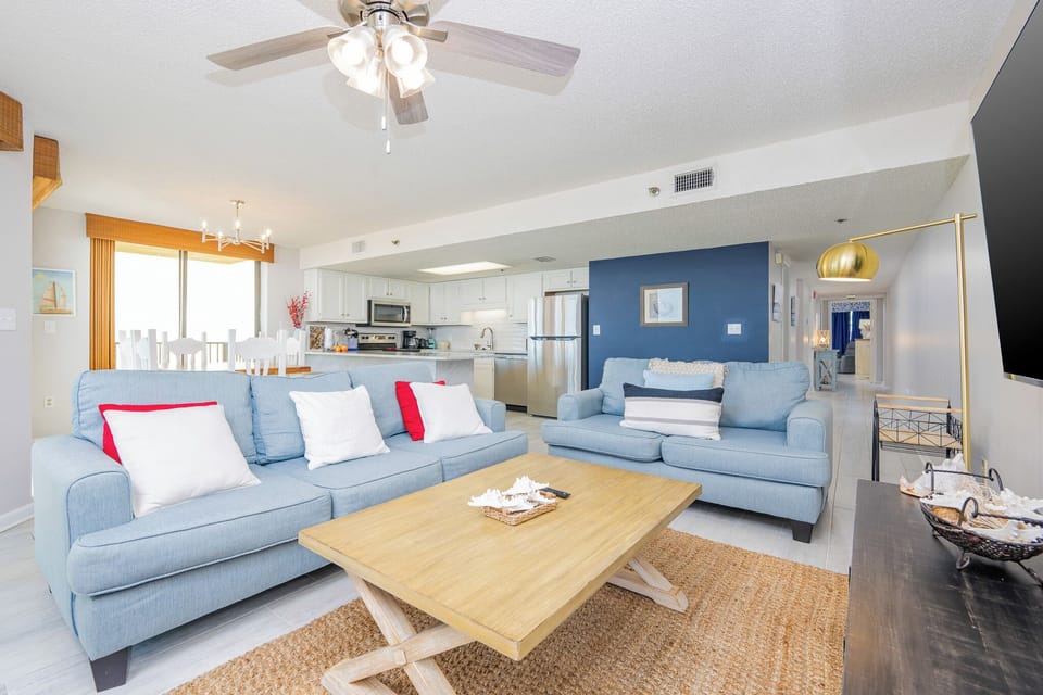 Bright living area featuring a light blue sofa with red accents, a wooden coffee table, and a view towards the dining area