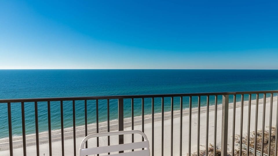 A serene view from the balcony showcases the tranquil blue waters and white sand beach below, inviting relaxation