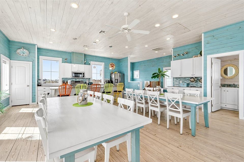 Your spacious kitchen and dining area welcomes gatherings with cheerful turquoise walls, white shiplap ceilings, and colorful seating for memorable meals together.