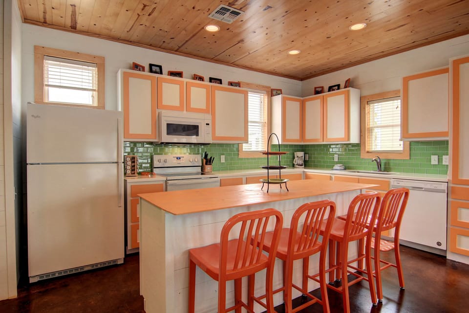 Cook meals in your bright kitchen featuring vibrant orange cabinets, green subway tile, and a spacious island with seating for four.