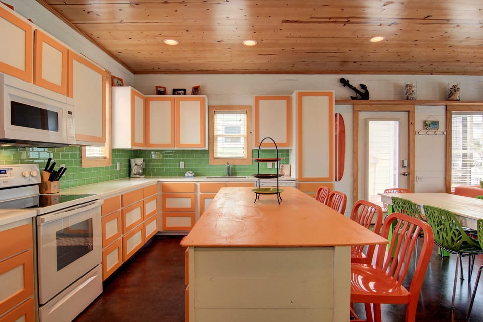 Your vibrant kitchen awaits with coral cabinets, emerald tile backsplash, and spacious island for cooking adventures.