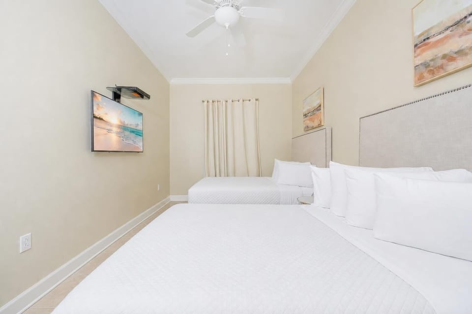 Soothing guest bedroom featuring two queen beds, soft linens, and a mounted TV