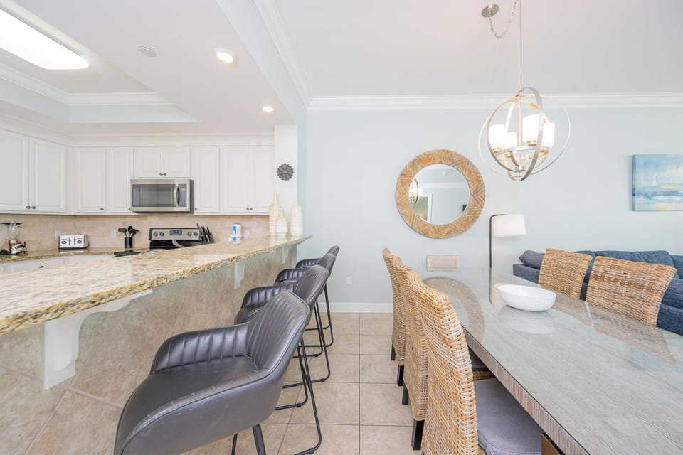 Gather around the sleek dining table with woven chairs, enjoying a seamless flow from the kitchen to the living area