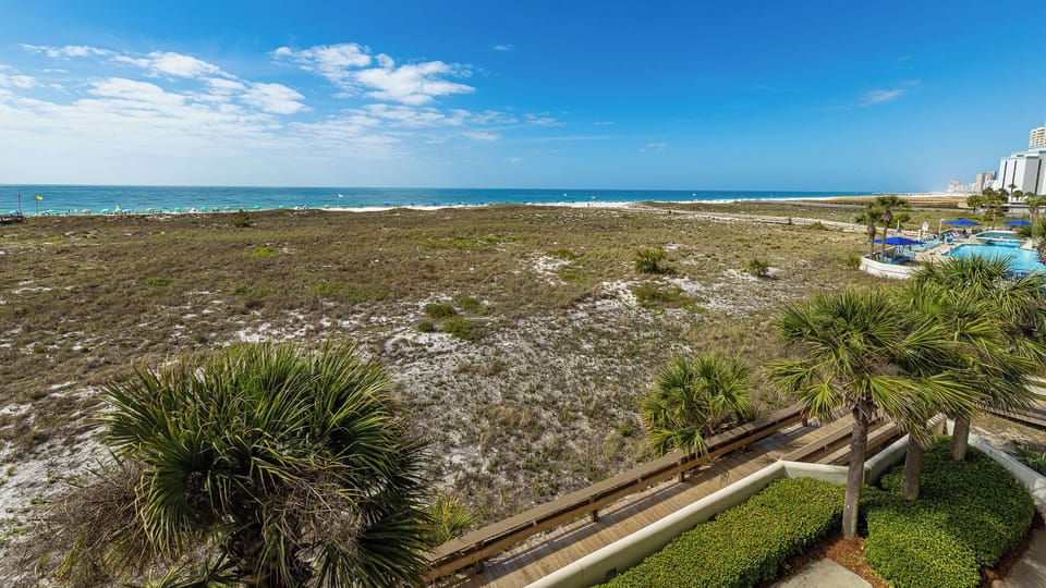 Poolside seating surrounds a tranquil pool area with a gazebo, leading to a scenic view of the beach and Gulf beyond