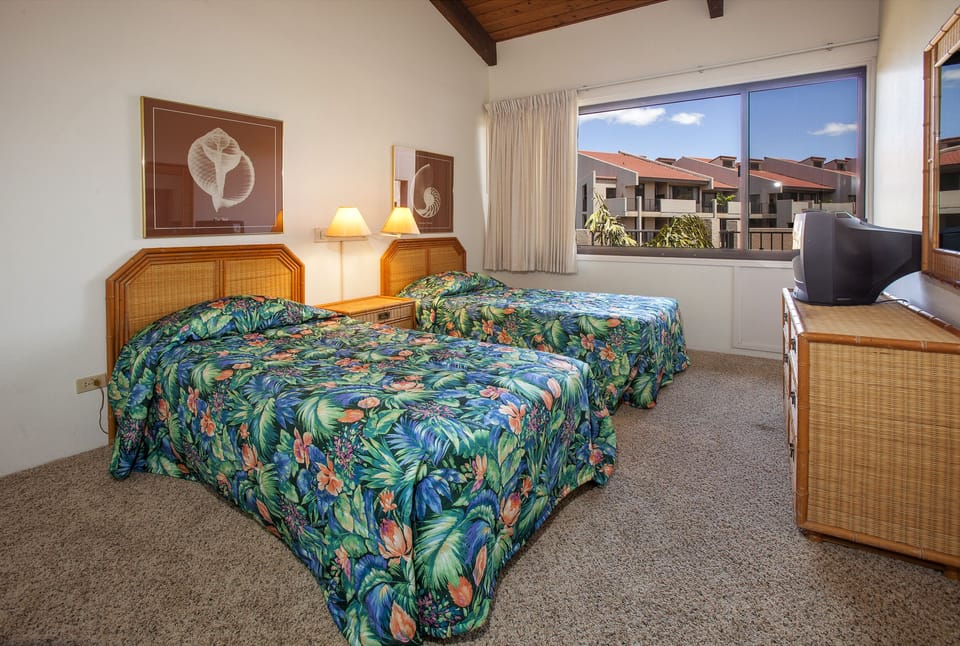 Unwind in your bright twin bedroom with tropical-print bedding, warm wood accents, and large windows framing peaceful neighborhood views. Your comfortable retreat awaits.