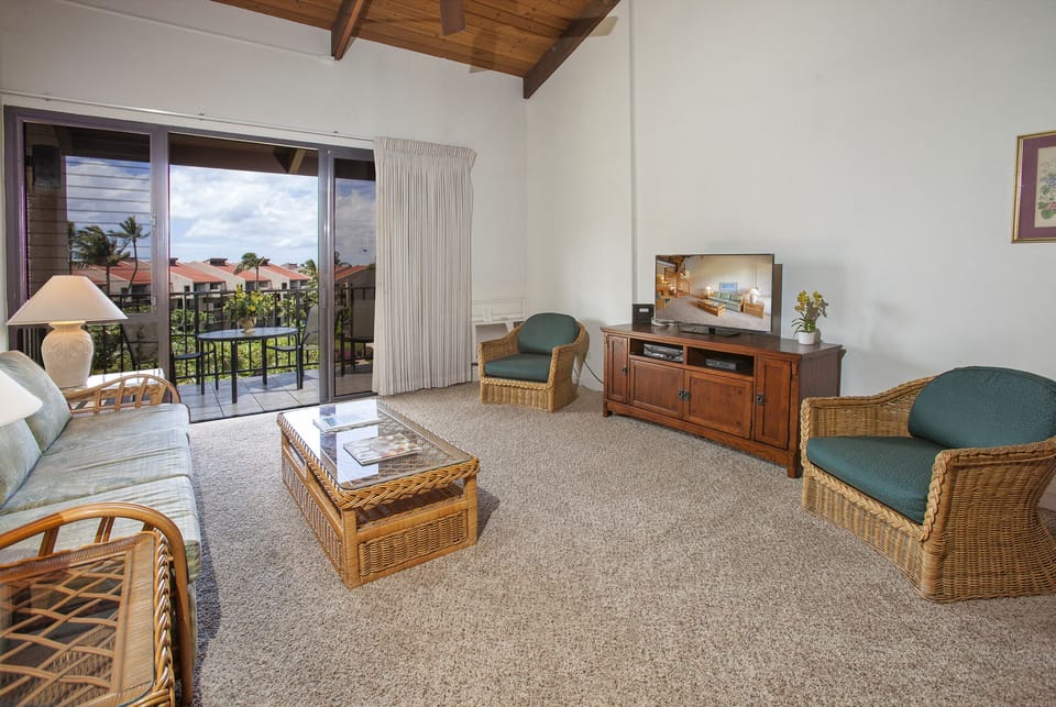 Relax in your bright, island-inspired living room with vaulted wood ceilings, comfy wicker seating, and tropical views from your private balcony overlooking lush surroundings.