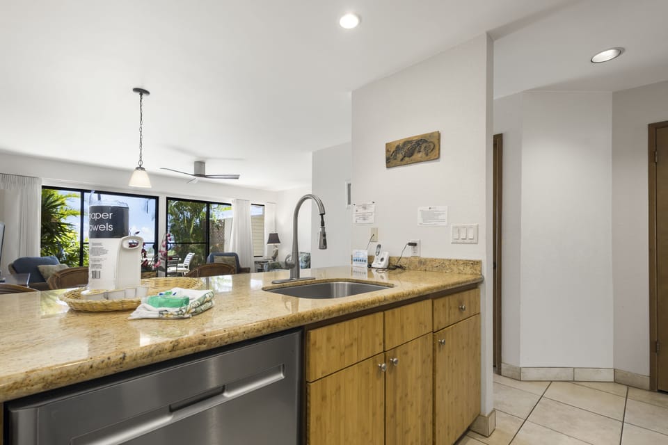 Your sunlit kitchen invites you to prepare meals at the sleek granite island while enjoying views of swaying palms outside. Open, airy, and thoughtfully equipped for your comfort.