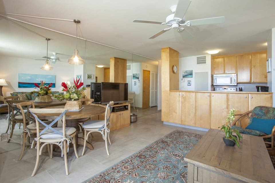 Step into your open-concept island retreat, where warm wood tones and tropical blooms welcome you to gather around the dining table, prep meals in the full kitchen, and relax under cooling ceiling fans.