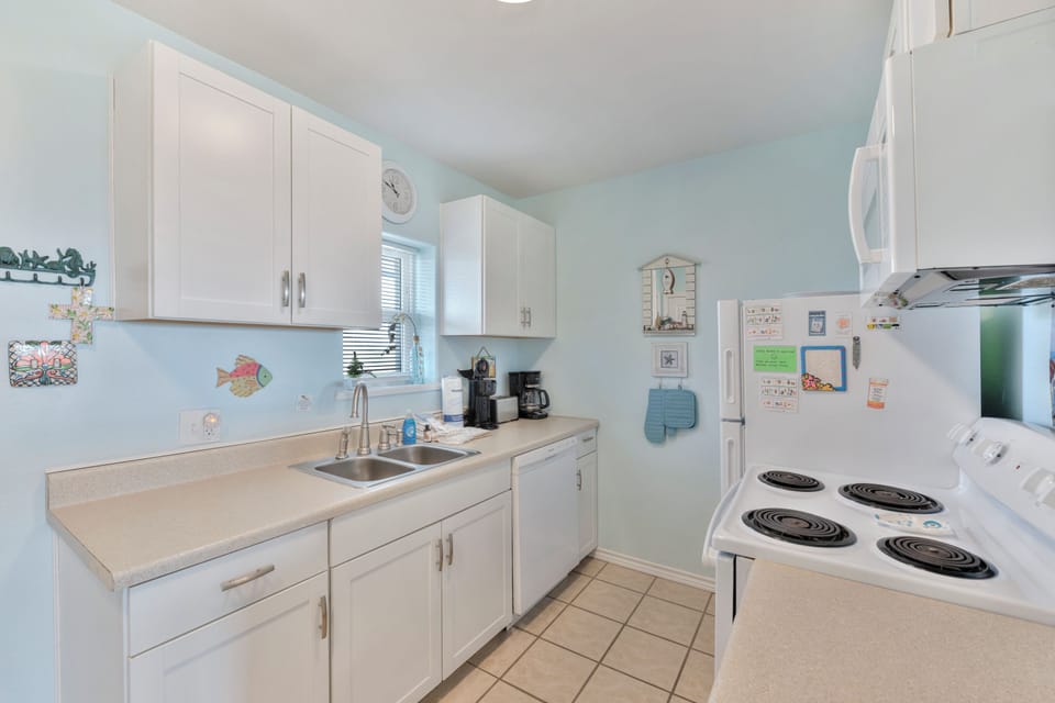 Your fully equipped kitchen awaits with bright white cabinets, modern appliances, and cheerful coastal touches that make meal prep feel like vacation.