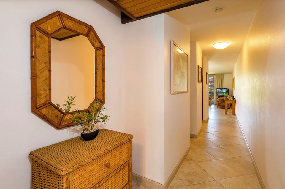A welcoming hallway leads you into the home, with warm tile floors, a handsome bamboo mirror, and a cozy living area beyond. Picture yourself arriving to this peaceful tropical retreat.