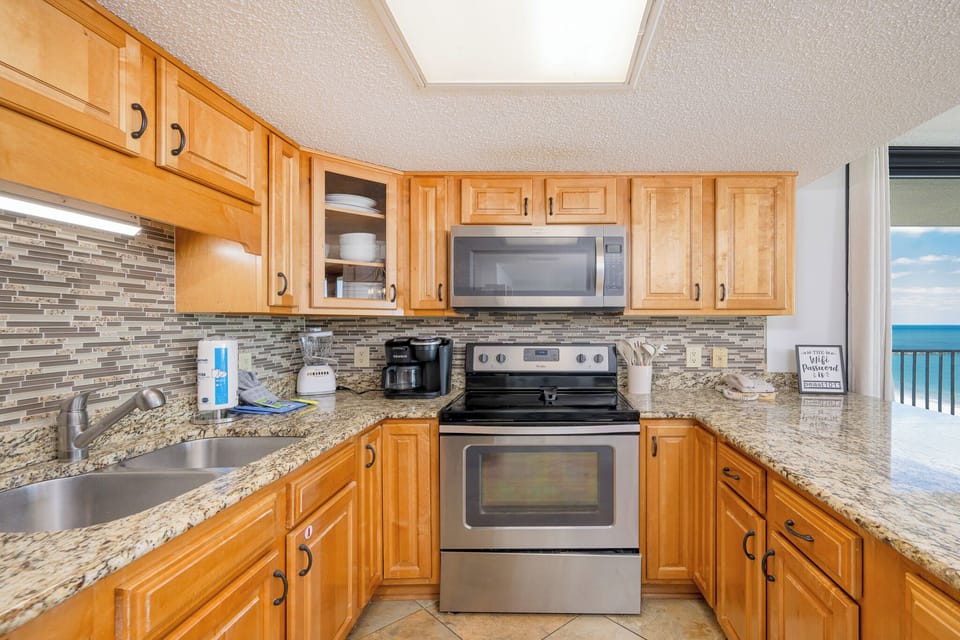 Prepare meals in this inviting kitchen featuring granite countertops, stainless appliances, and a view of the beach