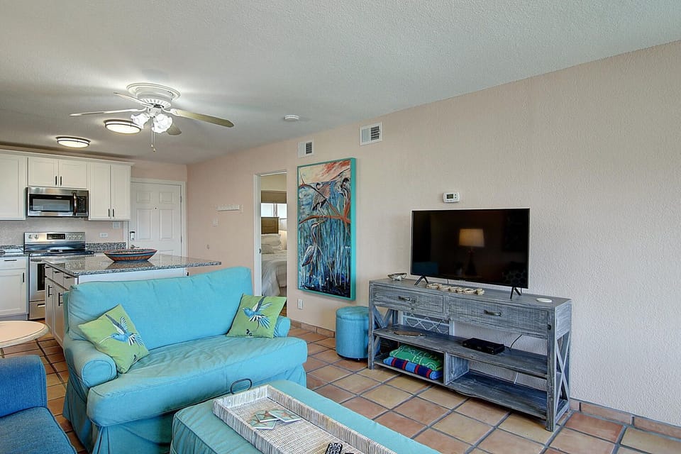 Relax in your bright, coastal-themed living space with turquoise seating and open kitchen—perfect for unwinding after beach adventures.