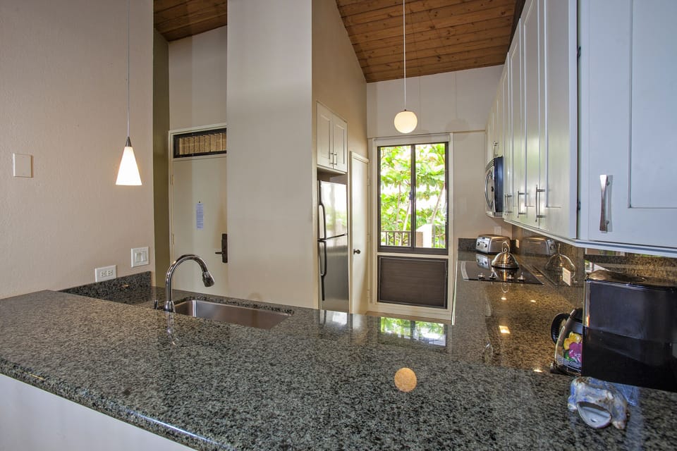 Your sleek kitchen features granite counters, modern appliances, and warm wood-beamed ceilings—a bright, inviting space where you can prepare meals while enjoying natural light streaming through the window.