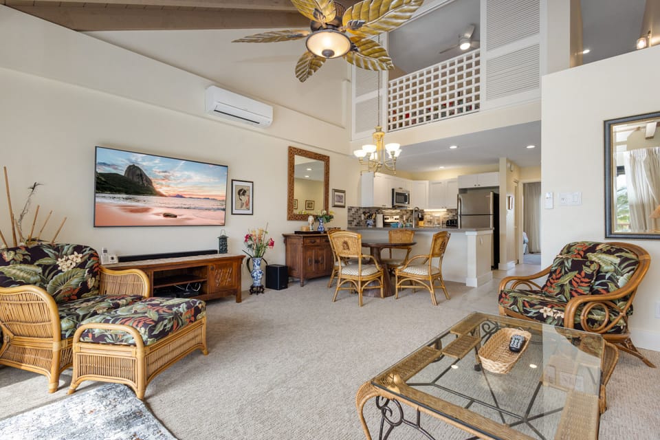 Unwind in your spacious open-concept living area, featuring tropical rattan furnishings, a large flatscreen TV, and a fully-equipped kitchen with modern appliances—perfect for your island getaway.