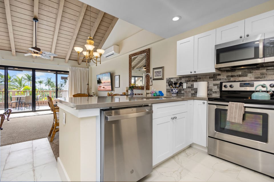 Cook with ease in your fully equipped kitchen featuring sleek stainless appliances, granite counters, and an open layout that flows to your private lanai with tropical views.