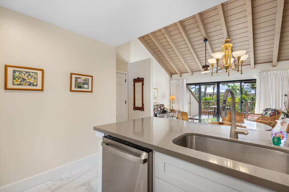 Your tropical retreat features a modern kitchen with sleek countertops and stainless appliances, opening to a bright living space with vaulted wood ceilings and balcony views of swaying palms.