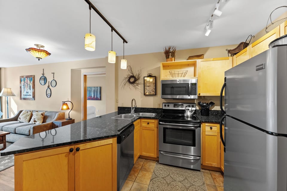 Your fully equipped kitchen features granite counters, stainless appliances, and opens to a cozy living space with mountain artwork.