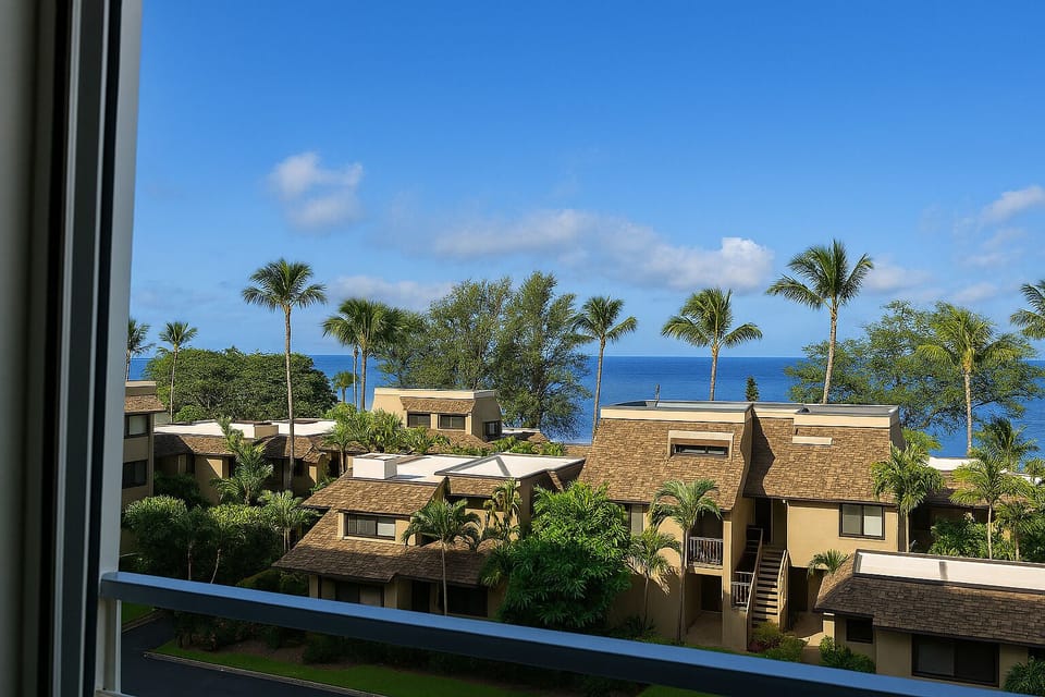 Tropical beachfront resort buildings nestled among palm trees with expansive ocean views on a clear sunny day.