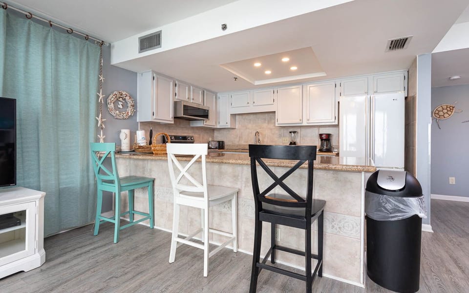 The kitchen features sleek cabinetry, granite countertops, stainless appliances, and a breakfast bar with colorful stools