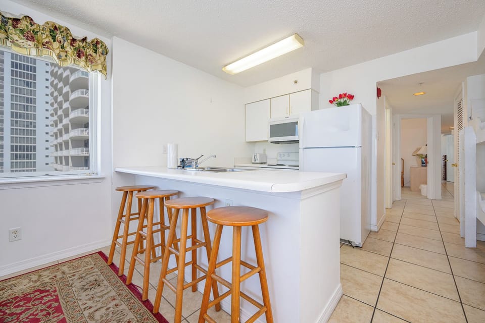 This kitchen features a bright, clean design with white cabinetry, a breakfast bar with wooden stools, and modern appliances