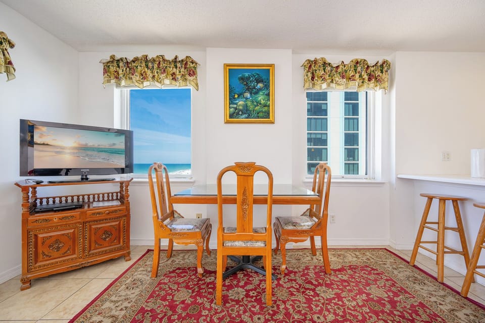 This inviting dining area features a wooden table, a TV, and a lovely view of the beachfront through sliding glass doors