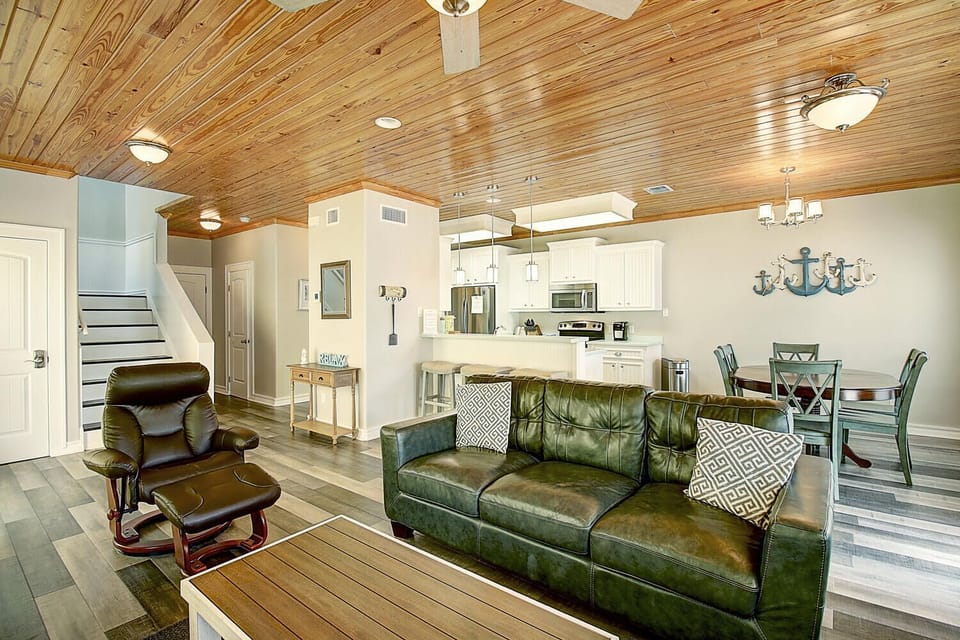 Relax in your spacious open-concept living area featuring rich leather seating, warm wood ceiling, and modern kitchen—perfect for unwinding after coastal adventures.