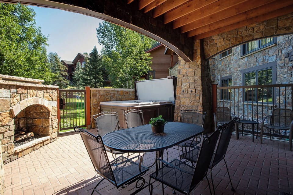 Your covered patio features a dining table and BBQ grill, perfect for outdoor meals with garden views and stone fireplace nearby.