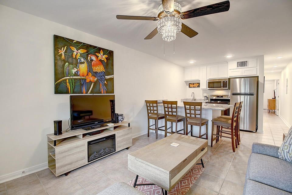Relax in your bright, modern living space featuring a fully equipped kitchen, dining area, and entertainment center with colorful tropical artwork.
