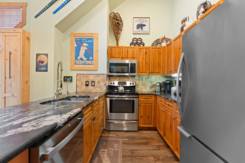 Your fully equipped kitchen features stainless steel appliances, warm wood cabinetry, and a cozy mountain-cabin vibe with vaulted ceilings—perfect for preparing meals together after a day of adventure.