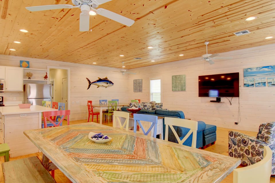 Gather around the colorful dining table in your bright, beach-themed living space with coastal décor and ceiling fans keeping you cool.