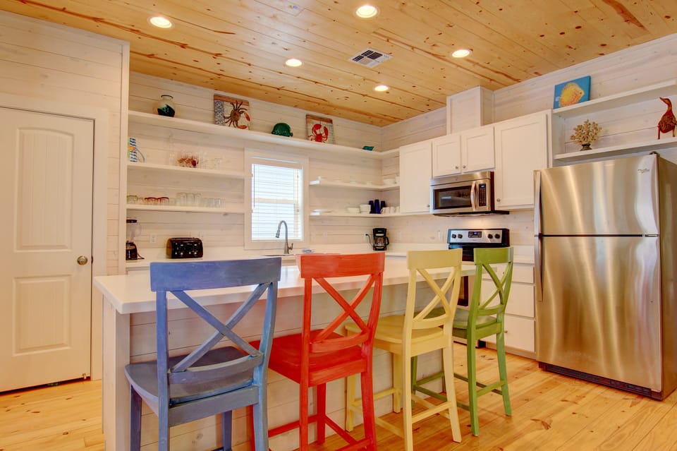 Your bright kitchen invites culinary adventures with colorful seating, open shelving, and modern appliances under charming wood ceilings.