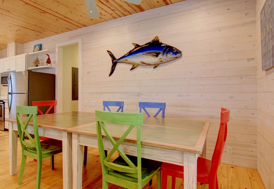 Gather around your vibrant dining table where colorful chairs and coastal charm create the perfect spot for memorable meals together.