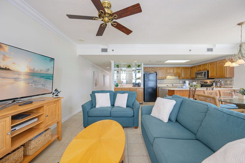 Cozy living space features a turquoise sofa, a dining table with rattan chairs, and a breakfast bar, perfect for beach days