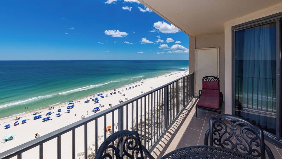 Black iron chairs and a cushioned lounger await you on your balcony with endless beach views and blue sky above